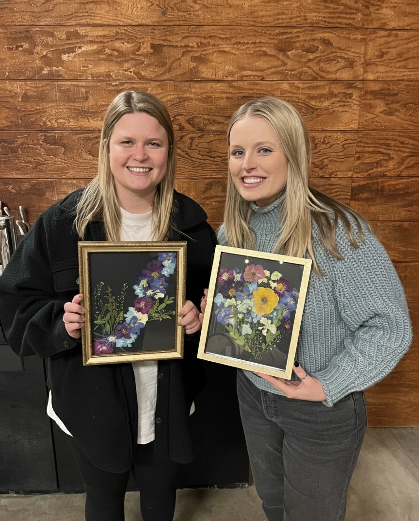 Pressed flower workshop showing floral designs, greenery, and flower presses on a work table.